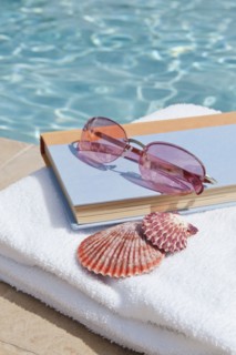 Book and sunglasses by swimming pool.
