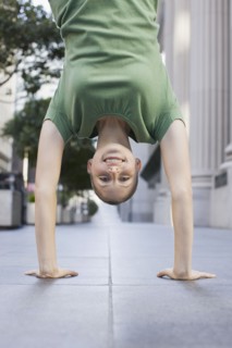 Businesswoman doing handstand on urban sidewalk. Photographe : PT Images