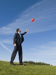 Businessman letting red balloon go.