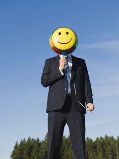 Businessman holding smiley face balloon over face.