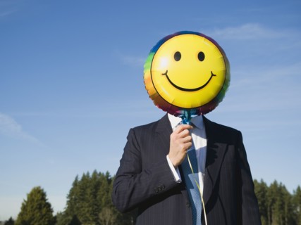 Businessman holding smiley face balloon over face.