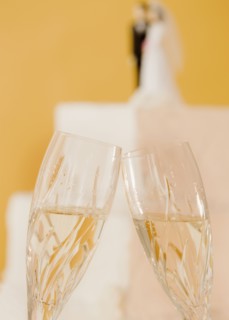 Close up of toasting champagne glasses and wedding cake. Photographe : Jamie Grill