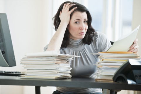 Stressed business woman holding paperwork in office.
