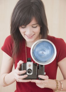 Young woman using camera, studio shot. Photographe : Jamie Grill