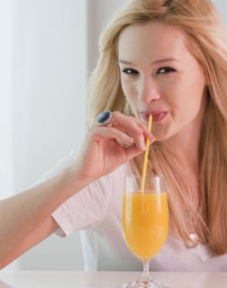 Portrait of young woman drinking orange juice. Photographe : Jamie Grill