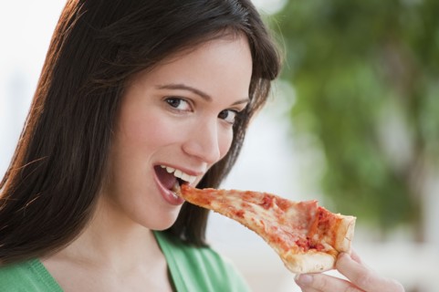 Portrait of woman eating pizza slice. Photographe : Daniel Grill