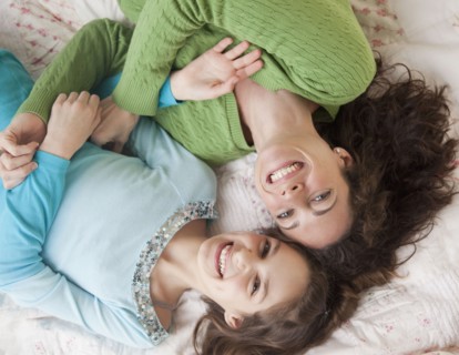 Mother and daughter (10-12 years) lying on bed, smiling, portrait, directly above. Photographe :