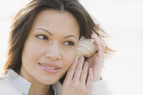 Close-up of woman listening to shell. Photographe : PT Images