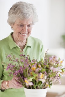 Senior woman setting flowers in vase.