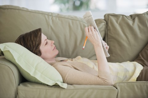 Woman lying on sofa with newspaper.
