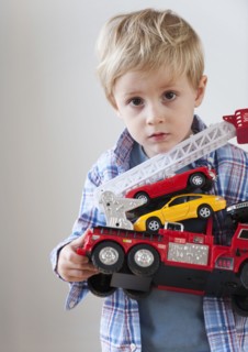 Portrait of boy (3-4) holding toy fire engine and cars.