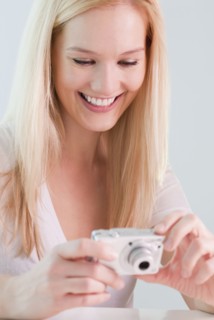 Young woman reviewing photos in digital camera, smiling. Photographe : Jamie Grill