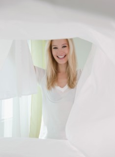Portrait of young woman making bed. Photographe : Jamie Grill