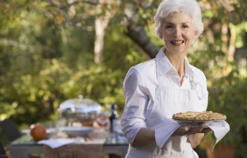 Senior woman standing in garden holding plate with pie. Photographe : mark edward atkinson