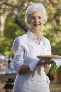 Senior woman standing in garden holding pie. Photographe : mark edward atkinson