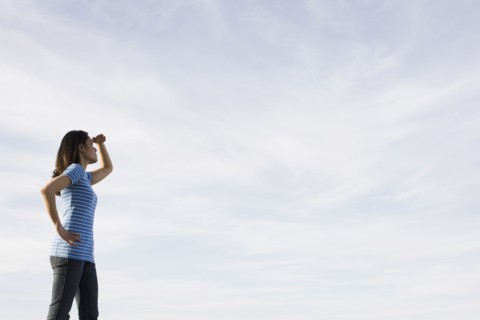 Woman shielding eyes against sky. Photographe : PT Images