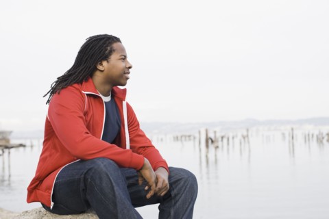 Teenage boy (16-17) with dreadlocks, sitting at waterfront, San Francisco, California, USA.