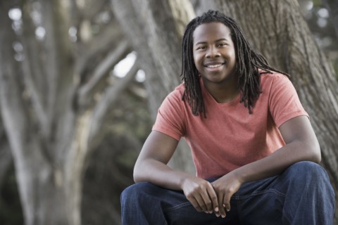 Portrait of teenage boy (16-17) with dreadlocks, sitting in park. Photographe : PT Images