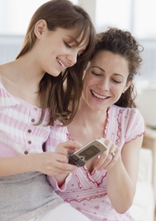 Daughter (10-12 years) teaching mother how to send text messages. Photographe : Jamie Grill