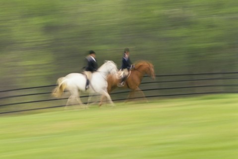 Two people riding on horses on field, blurred motion. Photographe : Stewart Cohen