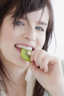 Portrait of young woman eating kiwi fruit. Photographe : Jamie Grill