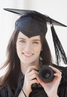 Portrait of young woman in graduation gown holding camera. Photographe : Jamie Grill