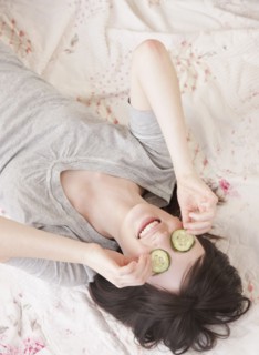 Young woman lying in bed with cucumber face mask. Photographe : Jamie Grill