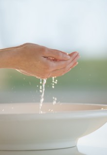 Water dripping from cupped hands over bowl.