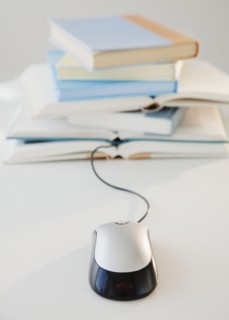 Computer mouse near pile of books, studio shot. Photographe : Jamie Grill
