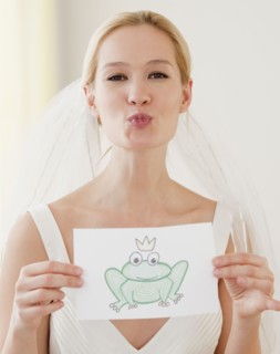 Portrait of young bride blowing kiss and holding drawing of frog prince. Photographe : Jamie Grill