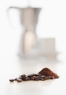 Heap of coffee beans with coffee cups in background.