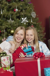 Sisters sitting in front of Christmas tree and holding Christmas gifts. Photographe : Sarah M.