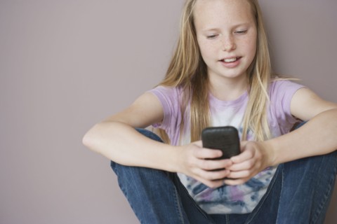 Girl (10-12) sitting and text messaging. Photographe : Sarah M. Golonka