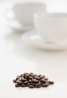 Heap of coffee beans with coffee cups in background.