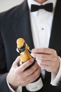 Champagne bottle being opened by a man in a tuxedo.
