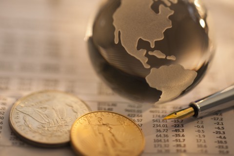 A globe on business papers with some coins.