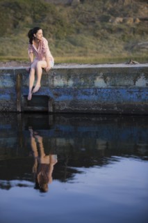 A woman sitting on a stone wall by water