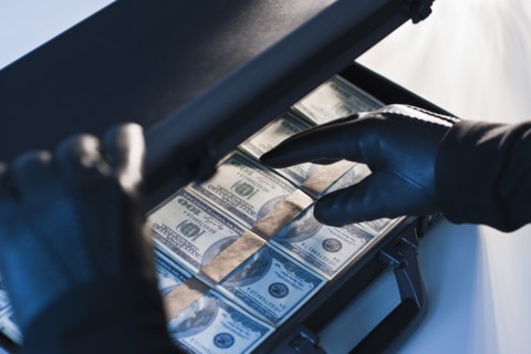 Money in a briefcase with gloved hands.