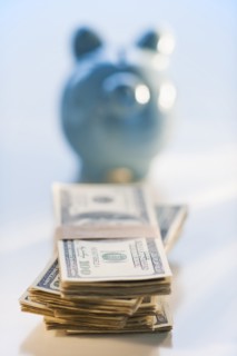 Bank notes and coins by a piggy bank.
