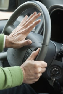 A hand honking a horn in a car.