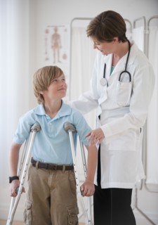 Female doctor assisting boy on crutches.