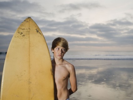 Boy standing beside surfboard