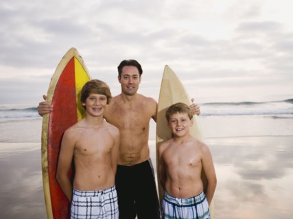 Father and sons standing with surfboards