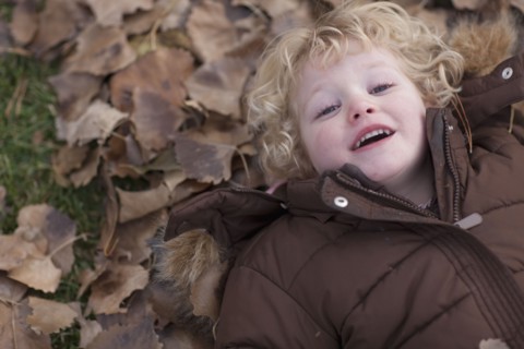 Young girl lying down on leaves. Photographer: Dan Bannister
