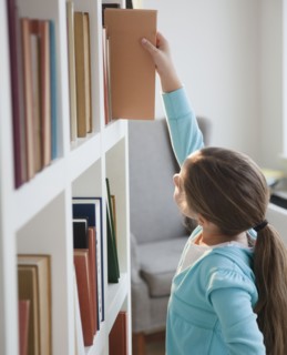 Young girl taking book of bookshelf. Photographer: Jamie Grill