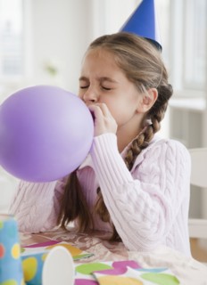 Young girl blowing up balloon. Photographer: Jamie Grill