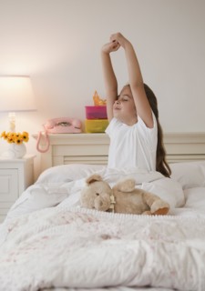 Young girl stretching in bed. Photographer: Jamie Grill