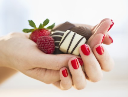 Hand holding chocolates a raspberry and a strawberry.
