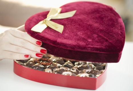 Hand opening a velvet heart shaped box of chocolates.