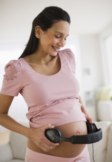 Pregnant woman holding headphones on her belly.